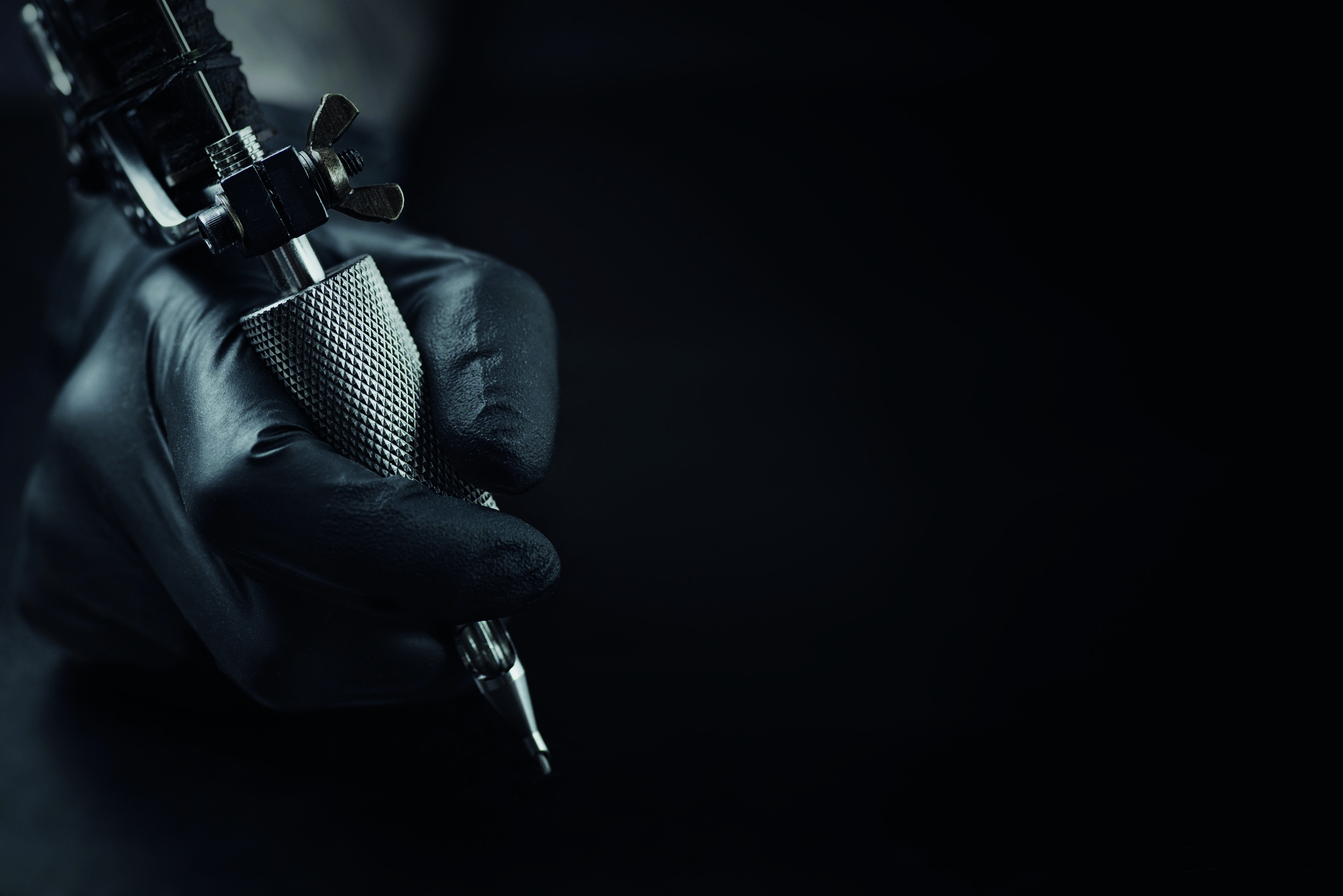 Eine Hand mit schwarzen Handschuhen hält eine Tattoo-Maschine – das Instrument für individuelle und saubere Tätowierkunst im Witoo Tattoo-Studio Deggendorf.
